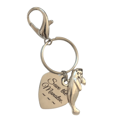 A photo of the Mother's Day Charm, which features a manatee-shaped charm, a heart-shaped charm with "Save the Manatee" written in script, attached to a claw-style clasp.