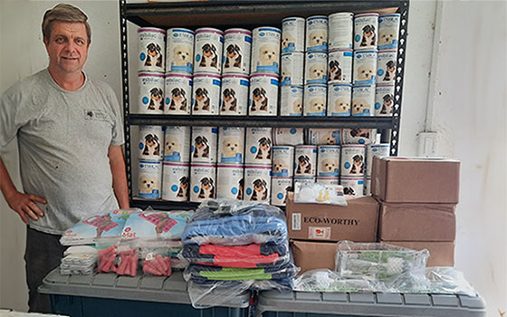 Paul Walker of Wildtracks stands to the left of shelving that contains several containers of milk replacement formula. In front of the shelf are bins, towels, and other supplies needed to help rehabilitate manatees.