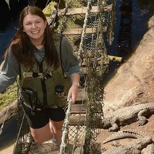 A photo of Kayleigh Summers walking across a rope and plank bridge over alligators.