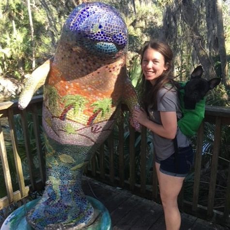 A photo of Stephanie Cohen in front of a manatee statue at Blue Spring State Park with her dog.